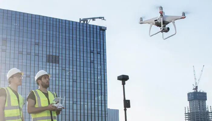 Два оператора в касках запускают квадрокоптер Phantom 4 RTK у здания