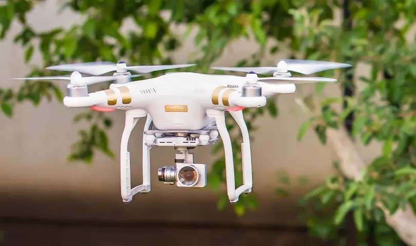 Белый квадрокоптер DJI Phantom с камерой среди зелени