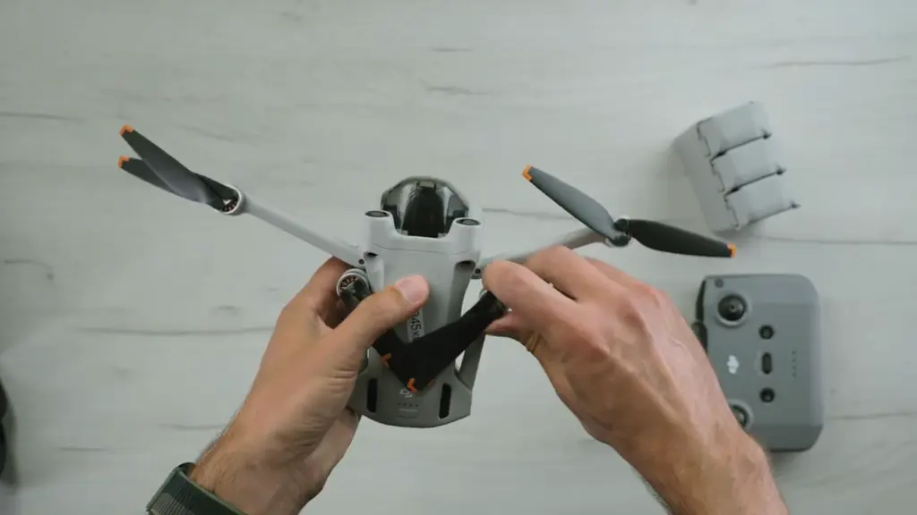 Руки держат квадрокоптер DJI Mini 3 Pro рядом с пультом и аккумуляторами